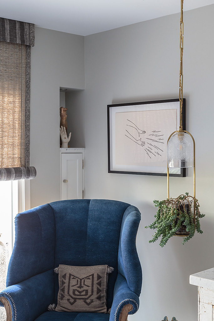 Blue wingback chair with woven Roman shade and brass pendant — architectural window layering by Bronwyn Poole