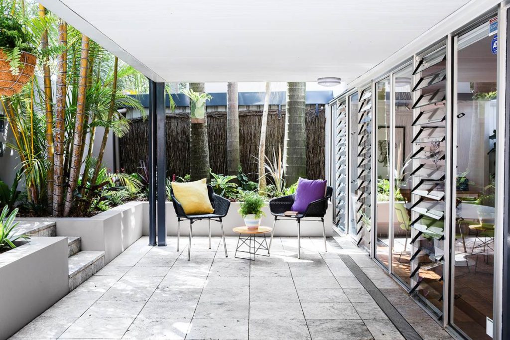 covered patio with tropical garden black woven chairs and stone pavers in Los Angeles home