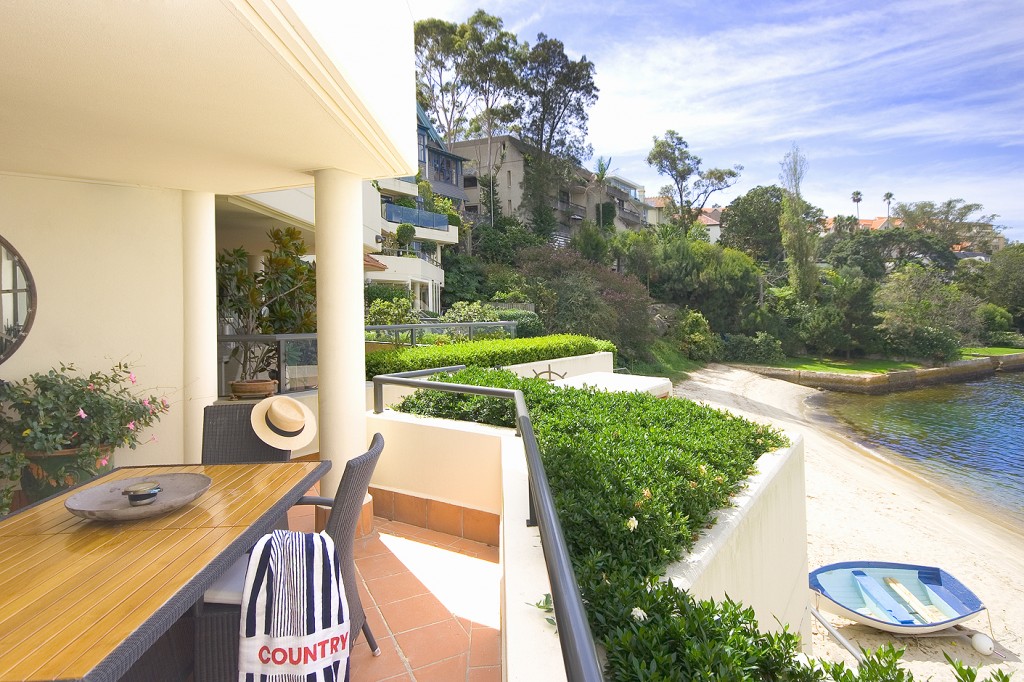 beachfront balcony with teak dining table wicker chairs and harbour view coastal outdoor living