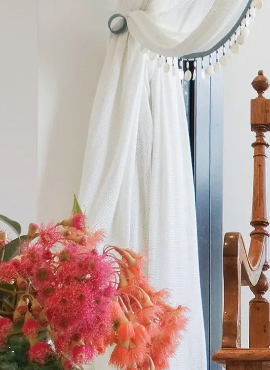 Native flowering gum arrangement in green vase with shell-trim curtain detail — bespoke window fabrication by Bronwyn Poole
