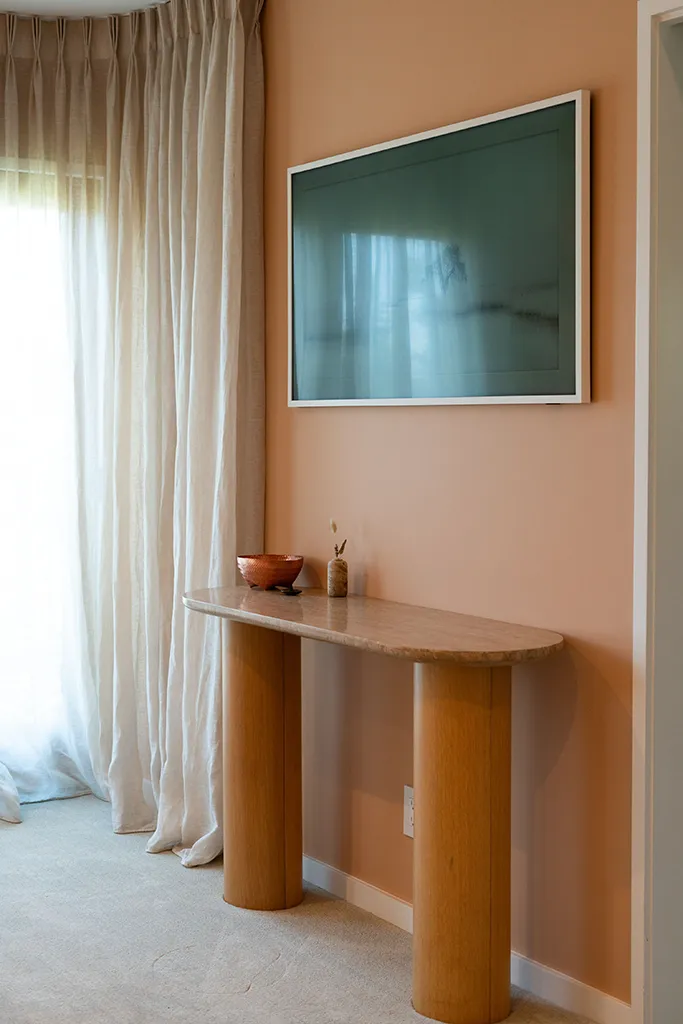 Floor-length linen curtain puddling on carpet beside oak console table with teal landscape artwork — architectural drapery detail by Bronwyn Poole