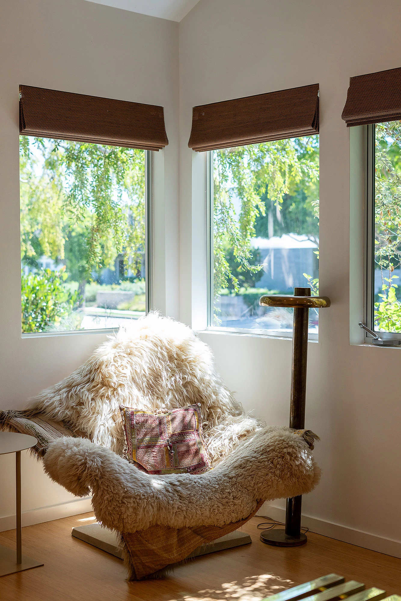 Sheepskin lounge chair in corner with woven Roman shades filtering garden light — integrated window design by Bronwyn Poole