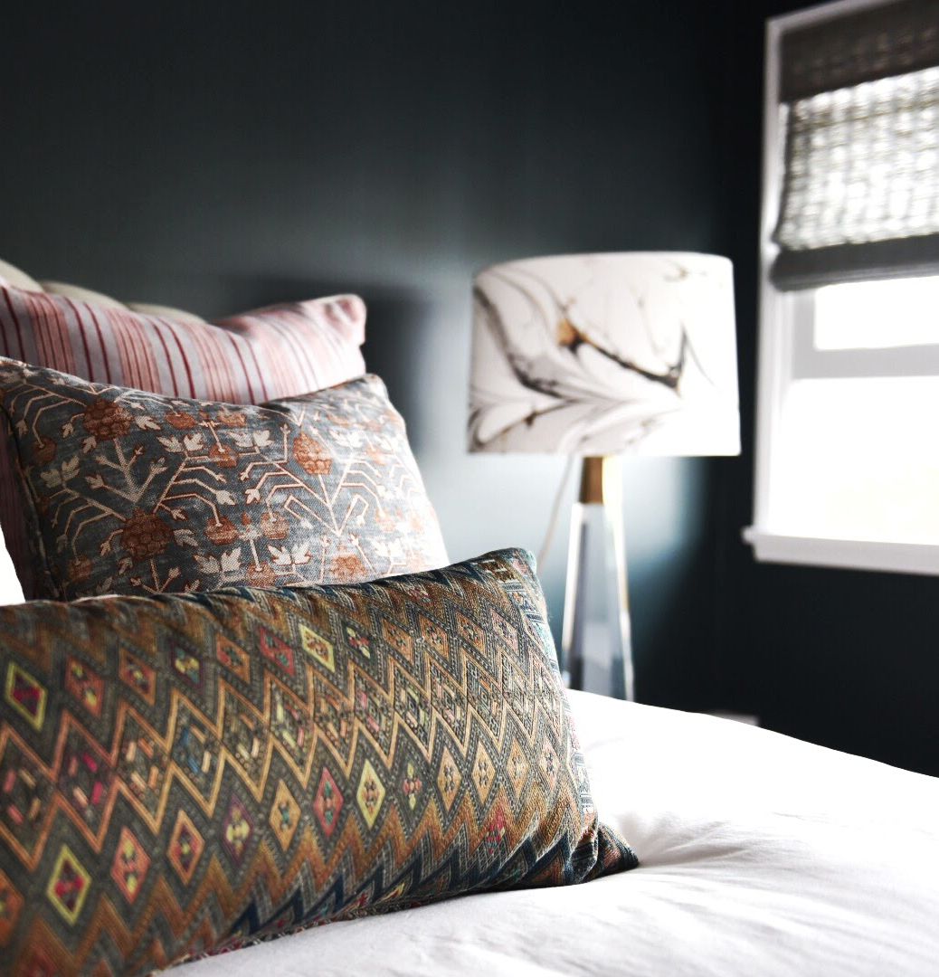 Moody dark bedroom with textured tribal pillows and botanical lampshade
