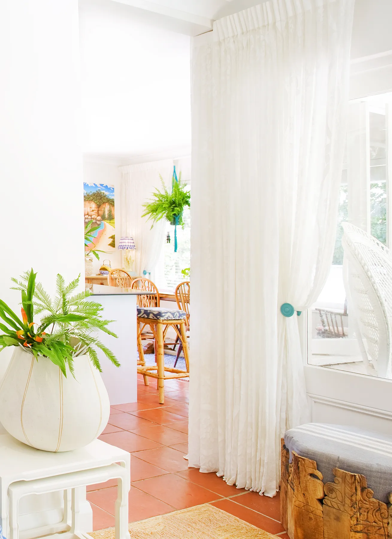 Sheer white linen curtains framing a living room with terracotta tiles and rattan dining — bespoke window design by Bronwyn Poole