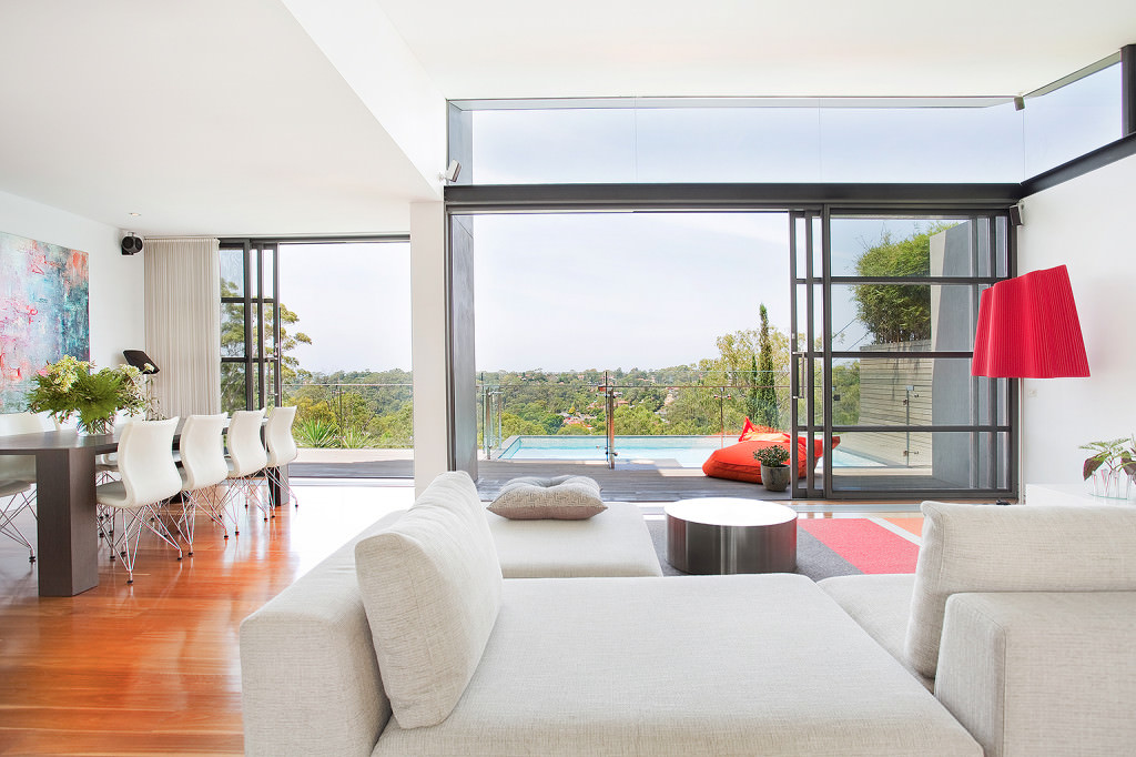 modern open plan living room with floor to ceiling glass doors opening to pool and hillside views