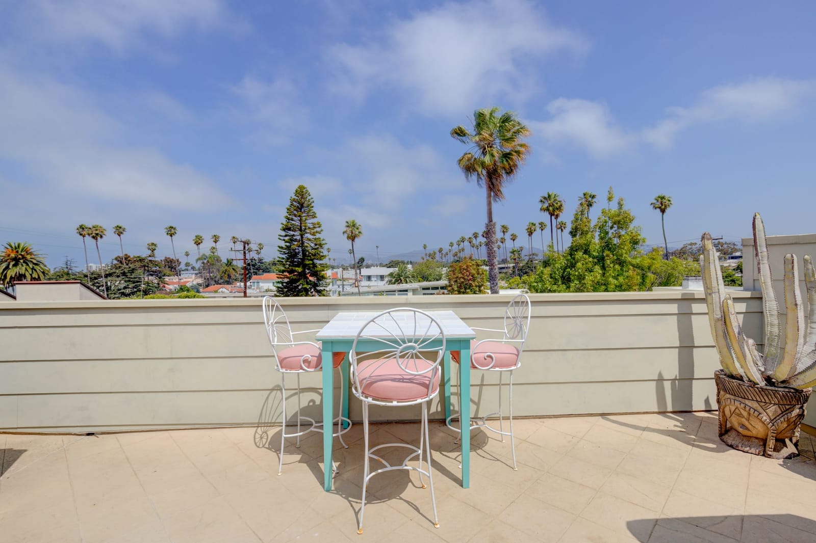 rooftop terrace with palm trees turquoise table and pink chairs overlooking California landscape