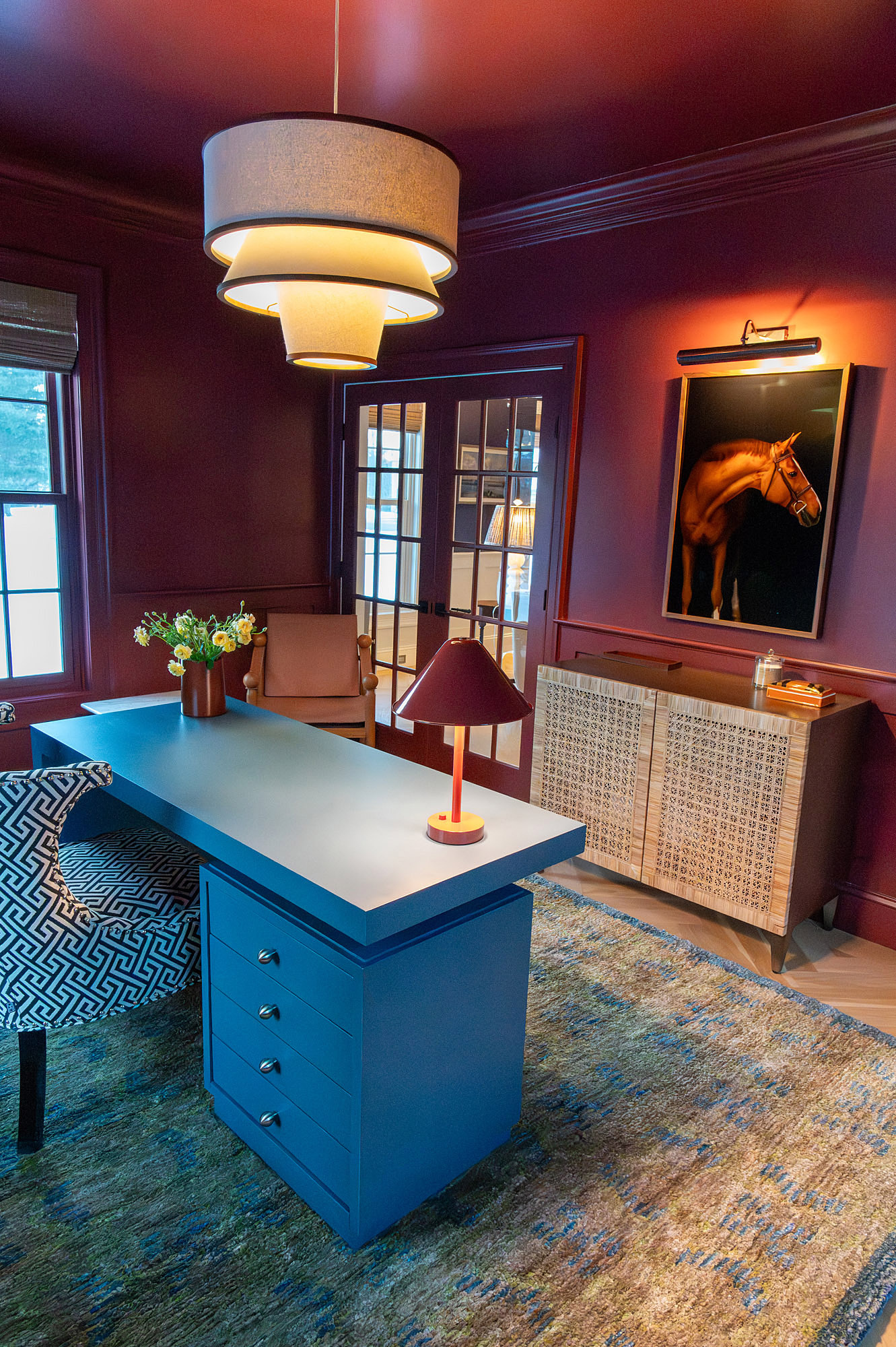 Den crimson walls equestrian portrait blue lacquered desk cane credenza tiered drum pendants leather chair greek key armchair blue rug — Bronwyn Poole Interiors