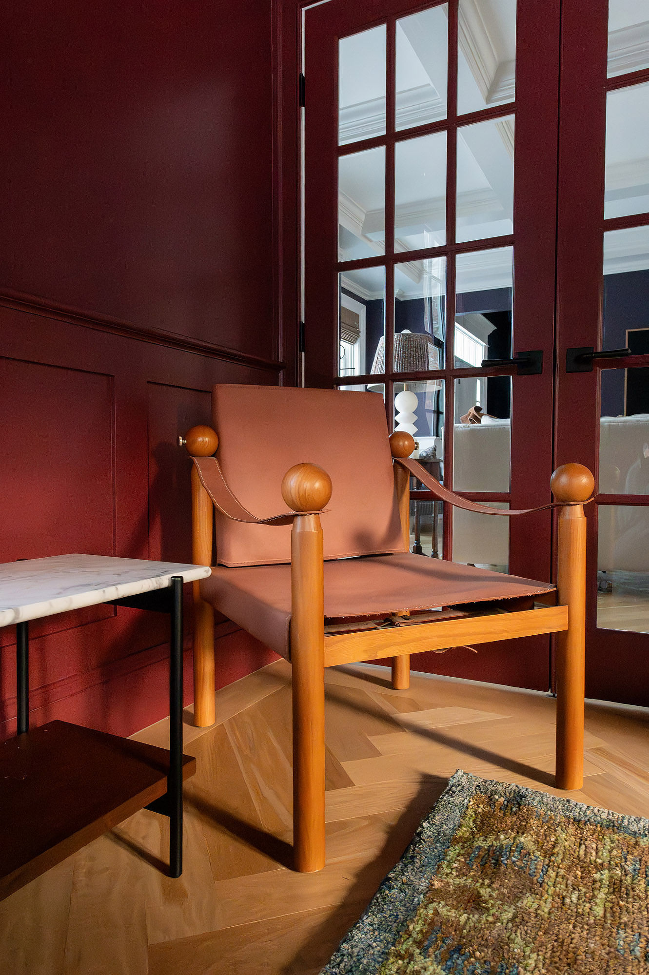 Den crimson walls tan leather safari chair walnut frame french doors marble side table vintage rug — Bronwyn Poole Interiors