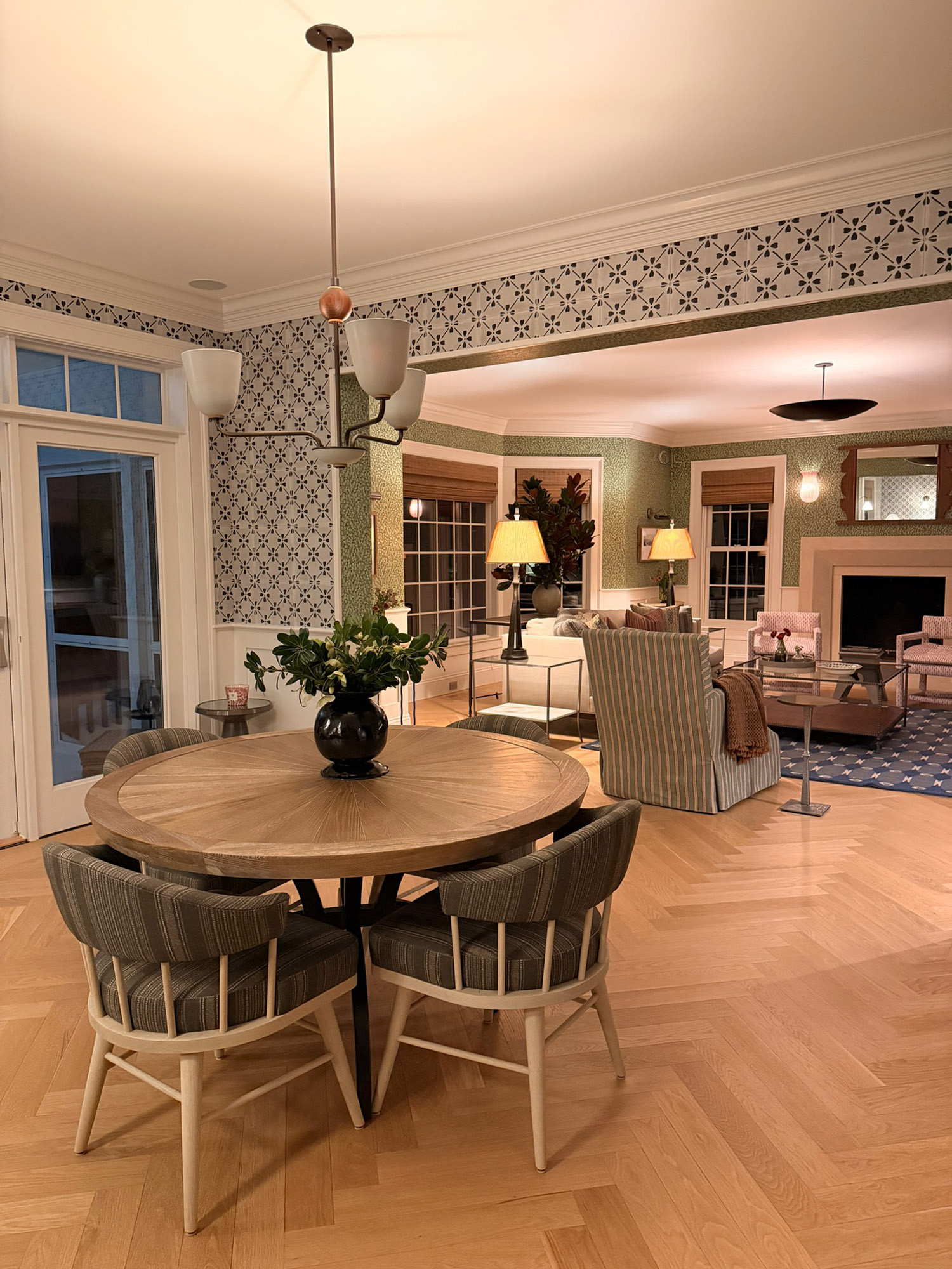 Dining area living room vista round oak table striped chairs floral tile frieze green leaf wallpaper fireplace evening — Bronwyn Poole Interiors