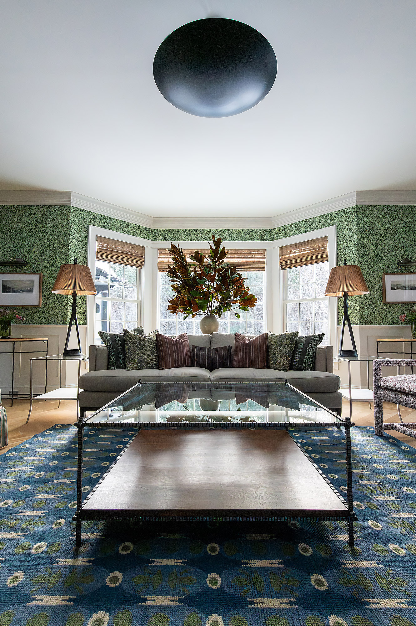 Living room bay window symmetrical view grey sofa magnolia branches floor lamps blue medallion rug green leaf wallpaper disc pendant — Bronwyn Poole Interiors Living room bay window symmetrical view grey sofa magnolia branches floor lamps blue medallion rug green leaf wallpaper disc pendant — Bronwyn Poole Interiors