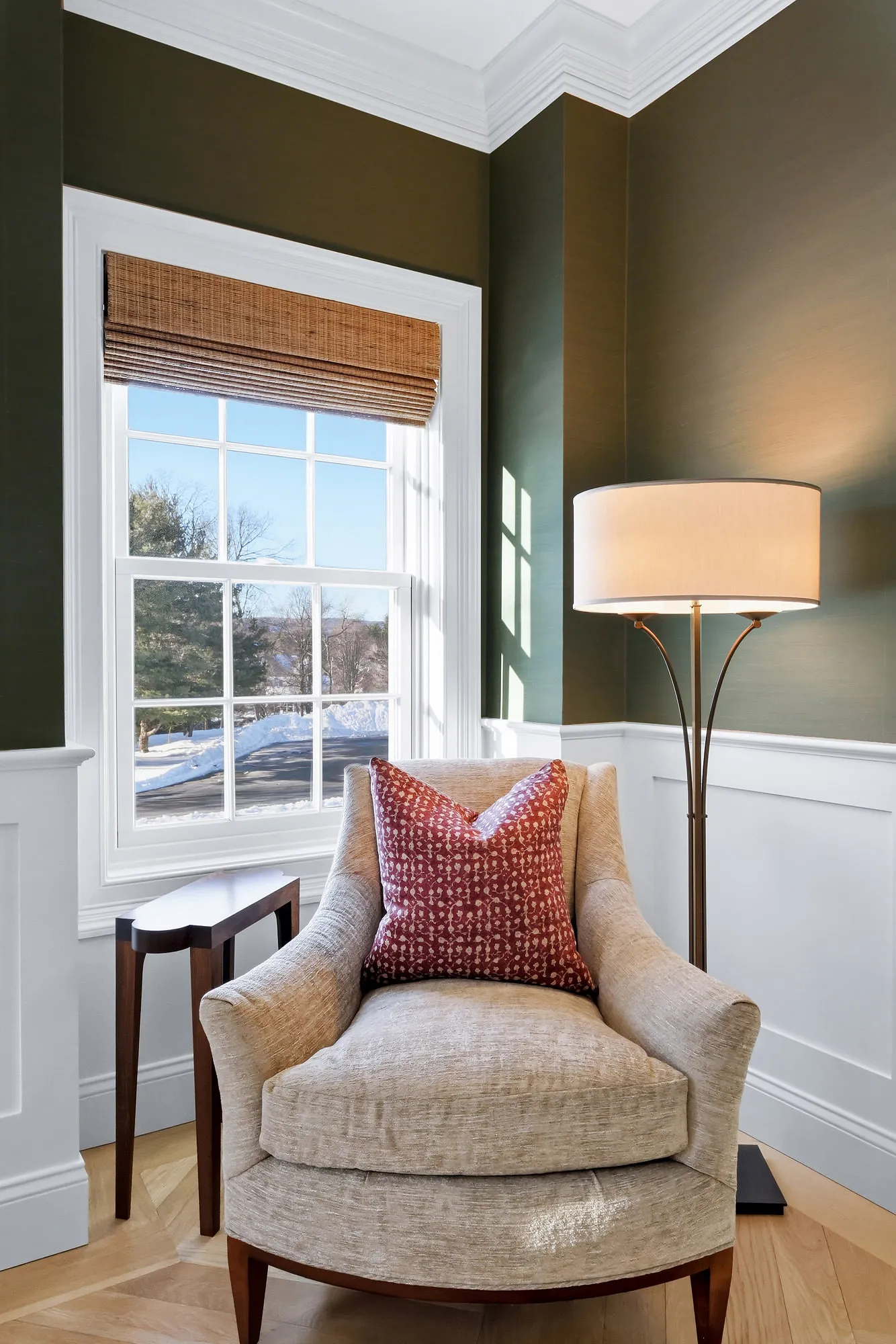 Olive green reading nook with armchair, woven Roman shade, and brass floor lamp — architectural window layering by Bronwyn Poole