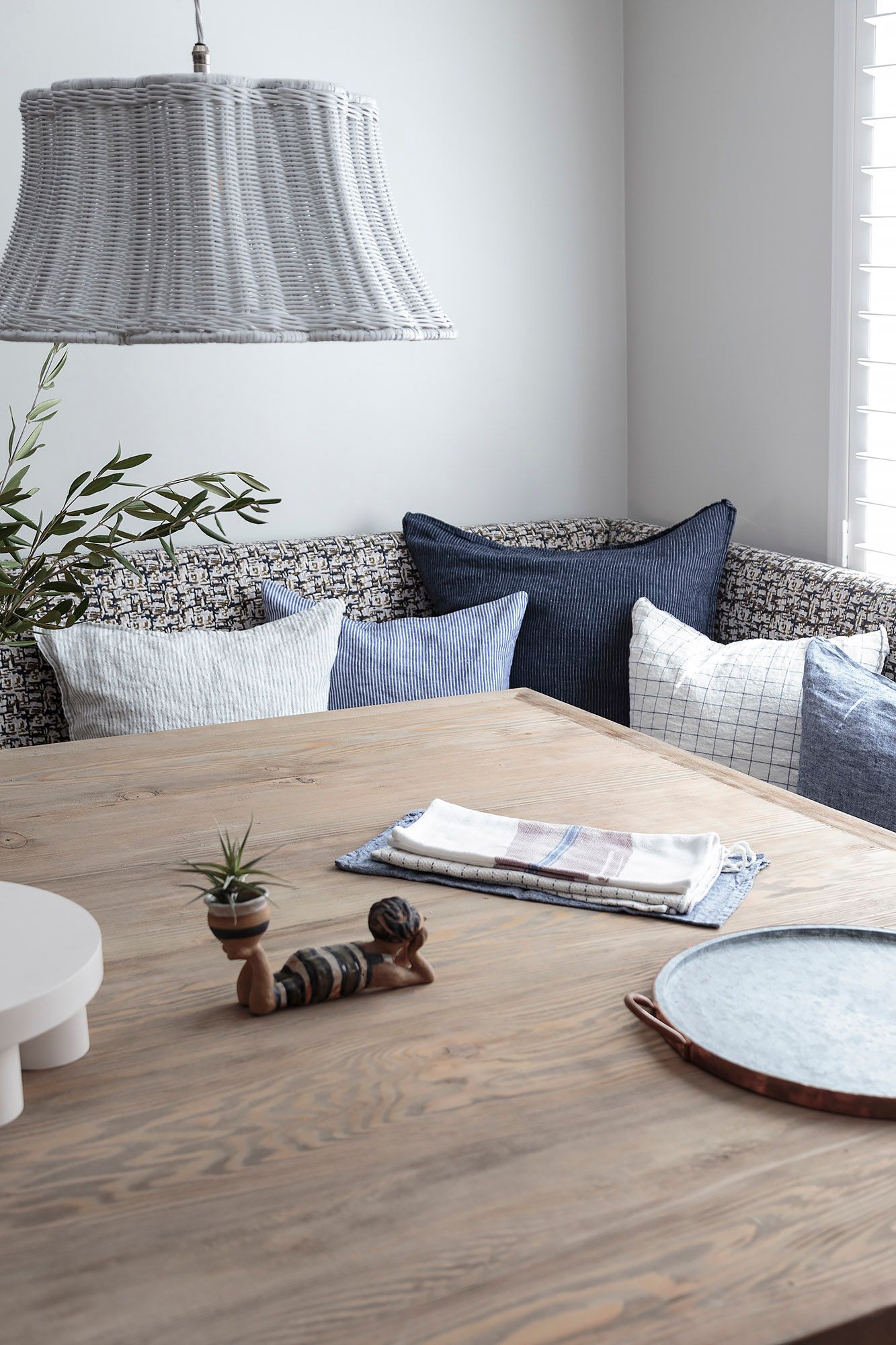 Blue and pale patterned pillows layered on a patterned upholstered banquette beside a timber dining table