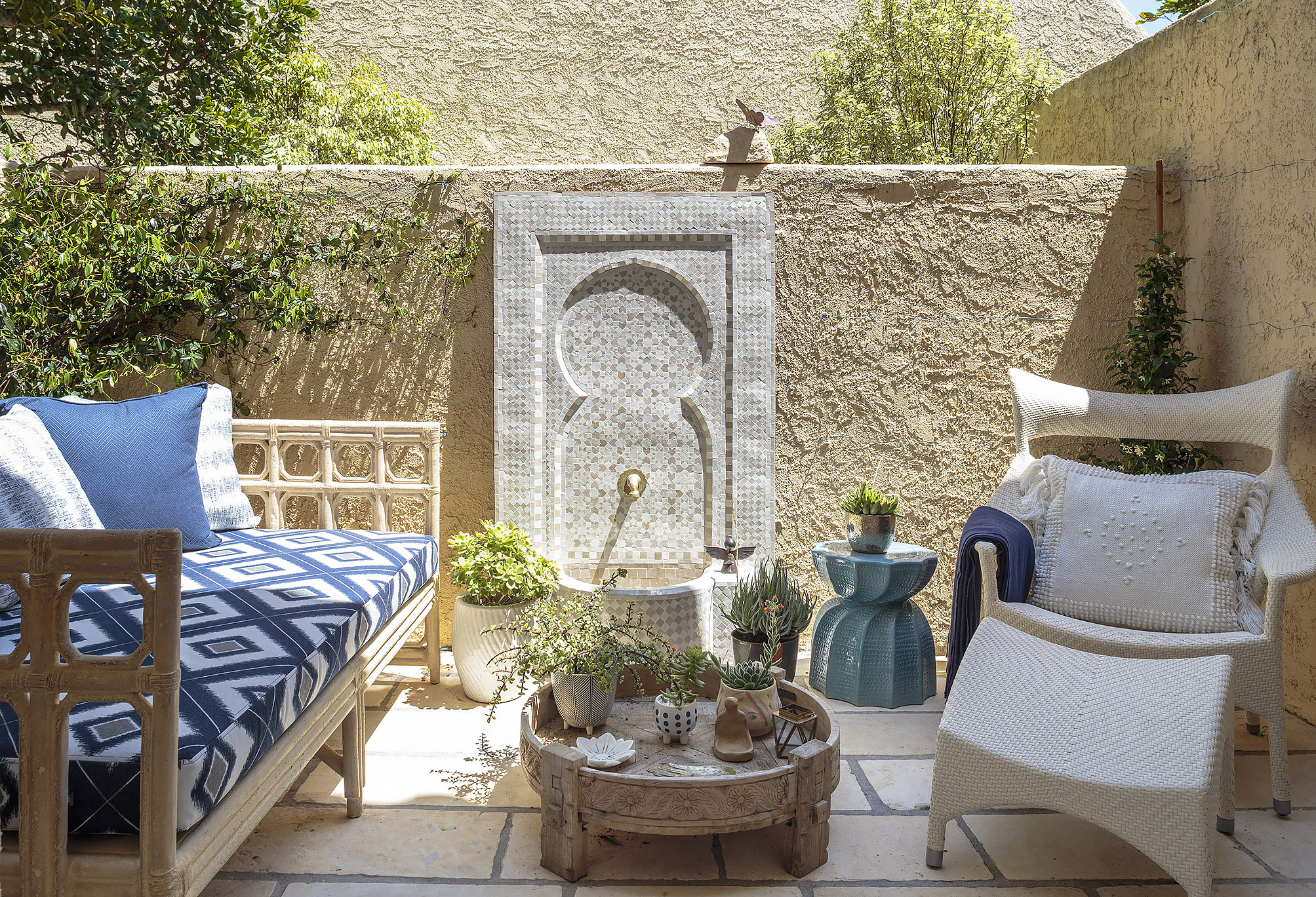 Moroccan inspired courtyard with mosaic fountain ikat daybed and carved table as outdoor living room
