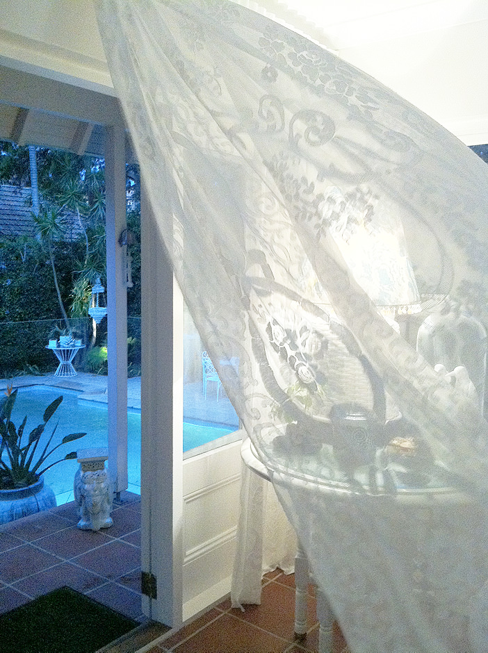 Billowing lace curtains framing a pool view — architectural light and movement by Bronwyn Poole